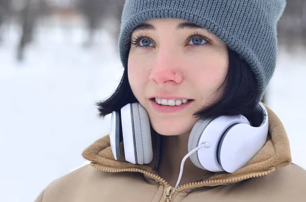 Güzellik kız kış orman içinde. Güzel genç esmer beyaz kadın şık kahverengi ceket ve sıcak siyah eşarp büyük beyaz kulaklık ile müzik dinlemek deldi.