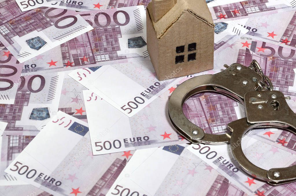 Scam with real estate. Cheating when buying or renting a house. Punishment for deception. A toy house with handcuffs on a many 500 purple euro banknotes