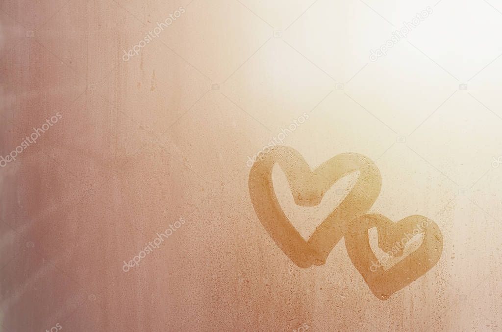 Couple of abstract blurred love heart symbol drawn by hand on the wet window glass with sunlight background. Template for Valentine Day postcards