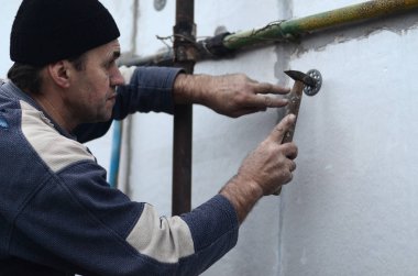 Yaşlı bir işçi Strafor duvarındaki bir plastik şemsiye bağlama içine bir dübel takunya. Genişletilmiş polistiren levhalar sabitleme işlemi. Bina cephe ısınma