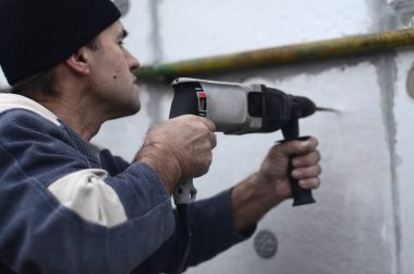 Yaşlı bir işçi bir plastik dübel takviye izleyen yüklemesi için styrofoam duvarında bir delik matkap. Delik duvara bir matkapla oluşturmak. Bina cephe Isınma