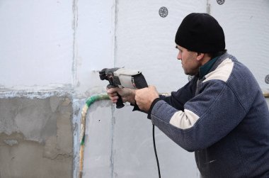 Yaşlı bir işçi bir plastik dübel takviye izleyen yüklemesi için styrofoam duvarında bir delik matkap. Delik duvara bir matkapla oluşturmak. Bina cephe Isınma