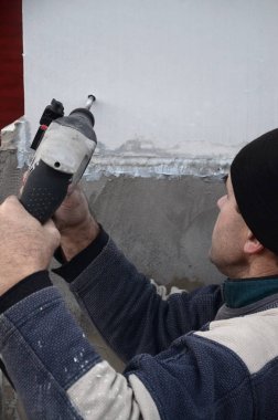 Yaşlı bir işçi bir plastik dübel takviye izleyen yüklemesi için styrofoam duvarında bir delik matkap. Delik duvara bir matkapla oluşturmak. Bina cephe Isınma