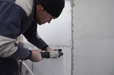Yaşlı bir işçi bir plastik dübel takviye izleyen yüklemesi için styrofoam duvarında bir delik matkap. Delik duvara bir matkapla oluşturmak. Bina cephe Isınma