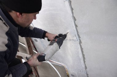 Yaşlı bir işçi bir plastik dübel takviye izleyen yüklemesi için styrofoam duvarında bir delik matkap. Delik duvara bir matkapla oluşturmak. Bina cephe Isınma