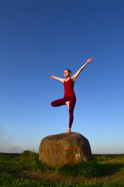 Siluet spor takım pratik Yoga akşam günbatımında pitoresk bir yeşil tepenin üzerinde genç sarışın kız. Egzersiz kavramı ve sağlıklı yaşam