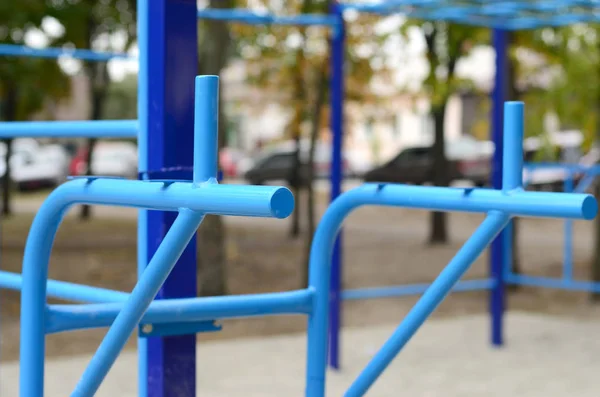 Sports bars in blue on the background of a street sports ground for training in athletics. Outdoor athletic gym equipment. Macro photo with selective focus and extremely blurred background