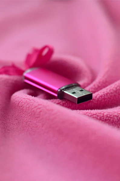 灿烂的粉红色 Usb 闪存卡与粉红色的弓躺在毯子柔软和毛茸茸的粉红色羊毛织物与许多浮雕褶皱 女性设计中的存储器存储装置 — 图库照片