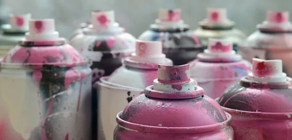 A lot of dirty and used aerosol cans of bright pink paint. Macro photograph with shallow depth of field. Selective focus on the spray nozzle