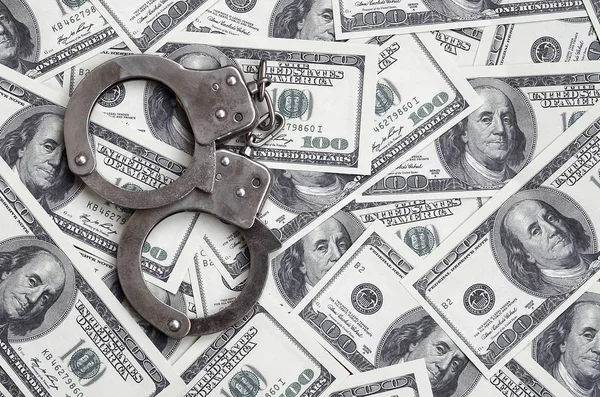 Police handcuffs lie on a lot of dollar bills. The concept of illegal possession of money, illegal transactions with US dollars. Economic Crime