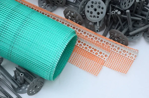 A set of construction items for the insulation of walls. Plastic dowels, a roll of mesh for the insulation of facades and a corner profile with a grid lie on the foam polystyrene surface — Stock Image Set Construction Items Insulation Walls Plastic Dowels Roll Mesh Insulation Stock Photo