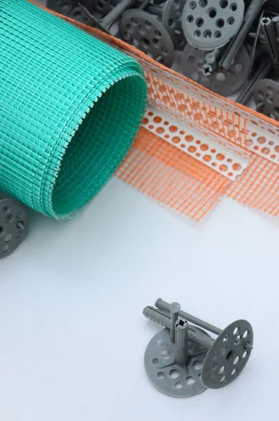 A set of construction items for the insulation of walls. Plastic dowels, a roll of mesh for the insulation of facades and a corner profile with a grid lie on the foam polystyrene surface — Stock Image Set Construction Items Insulation Walls Plastic Dowels Roll Mesh Insulation Stock Image