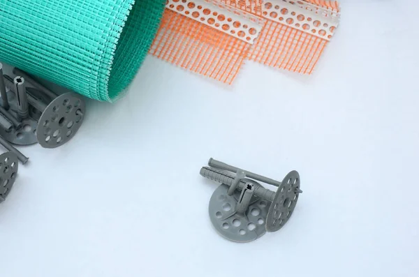 A set of construction items for the insulation of walls. Plastic dowels, a roll of mesh for the insulation of facades and a corner profile with a grid lie on the foam polystyrene surface — Stock Image Set Construction Items Insulation Walls Plastic Dowels Roll Mesh Insulation Stock Picture