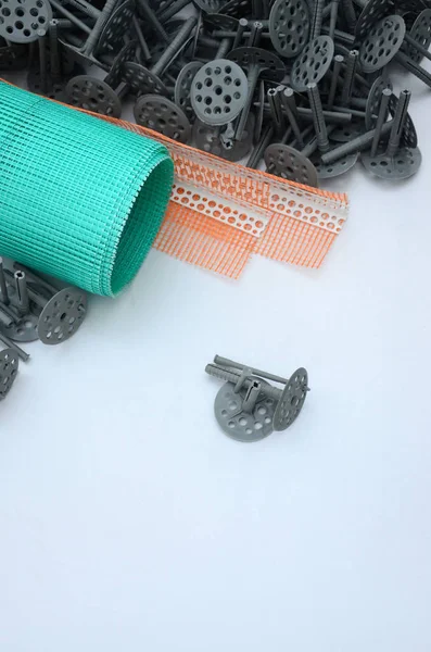 A set of construction items for the insulation of walls. Plastic dowels, a roll of mesh for the insulation of facades and a corner profile with a grid lie on the foam polystyrene surface — Stock Image Set Construction Items Insulation Walls Plastic Dowels Roll Mesh Insulation Stock Picture