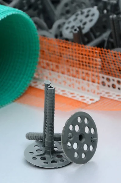 A set of construction items for the insulation of walls. Plastic dowels, a roll of mesh for the insulation of facades and a corner profile with a grid lie on the foam polystyrene surface — Stock Image Set Construction Items Insulation Walls Plastic Dowels Roll Mesh Insulation Stock Photo