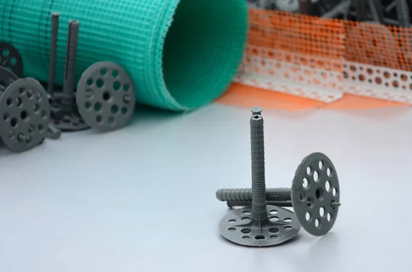 A set of construction items for the insulation of walls. Plastic dowels, a roll of mesh for the insulation of facades and a corner profile with a grid lie on the foam polystyrene surface — Stock Image Set Construction Items Insulation Walls Plastic Dowels Roll Mesh Insulation Stock Image