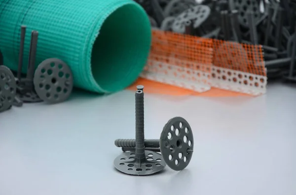 A set of construction items for the insulation of walls. Plastic dowels, a roll of mesh for the insulation of facades and a corner profile with a grid lie on the foam polystyrene surface — Stock Image Set Construction Items Insulation Walls Plastic Dowels Roll Mesh Insulation Stock Photo