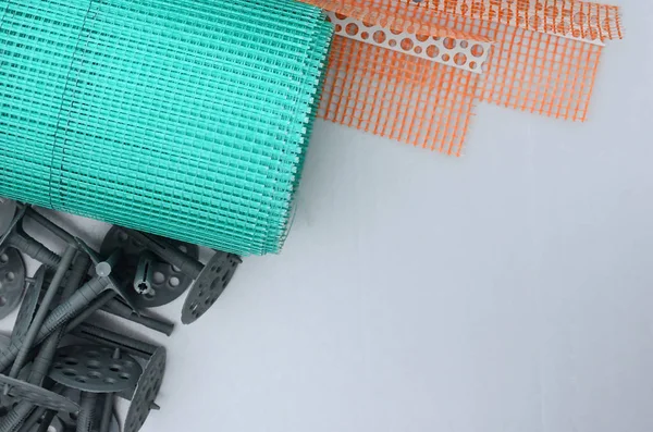 A set of construction items for the insulation of walls. Plastic dowels, a roll of mesh for the insulation of facades and a corner profile with a grid lie on the foam polystyrene surface — Stock Image Set Construction Items Insulation Walls Plastic Dowels Roll Mesh Insulation Stock Image
