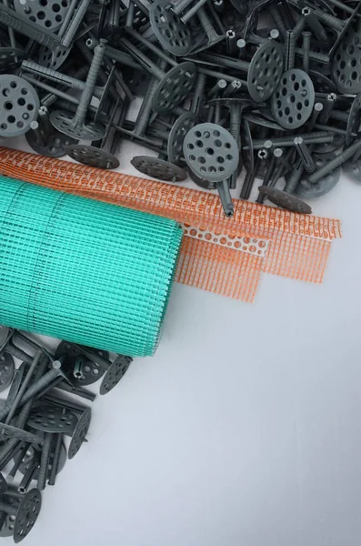 A set of construction items for the insulation of walls. Plastic dowels, a roll of mesh for the insulation of facades and a corner profile with a grid lie on the foam polystyrene surface — Stock Image Set Construction Items Insulation Walls Plastic Dowels Roll Mesh Insulation Stock Photo