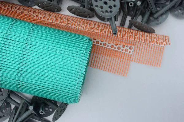 A set of construction items for the insulation of walls. Plastic dowels, a roll of mesh for the insulation of facades and a corner profile with a grid lie on the foam polystyrene surface — Stock Image Set Construction Items Insulation Walls Plastic Dowels Roll Mesh Insulation Royalty Free Stock Images