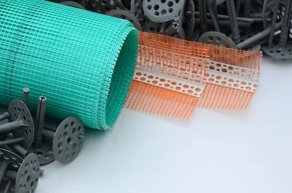 A set of construction items for the insulation of walls. Plastic dowels, a roll of mesh for the insulation of facades and a corner profile with a grid lie on the foam polystyrene surface — Stock Image Set Construction Items Insulation Walls Plastic Dowels Roll Mesh Insulation Stock Photo