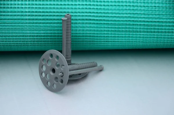 A set of construction items for the insulation of walls. Plastic dowels, a roll of mesh for the insulation of facades and a corner profile with a grid lie on the foam polystyrene surface — Stock Image Set Construction Items Insulation Walls Plastic Dowels Roll Mesh Insulation Royalty Free Stock Images