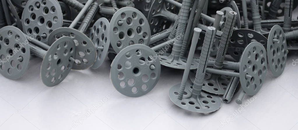 Background of many gray plastic dowels (fastening) for thermal insulation. A huge pile of plastic bolts with round holey hats lies on a gray foam polystyrene plate