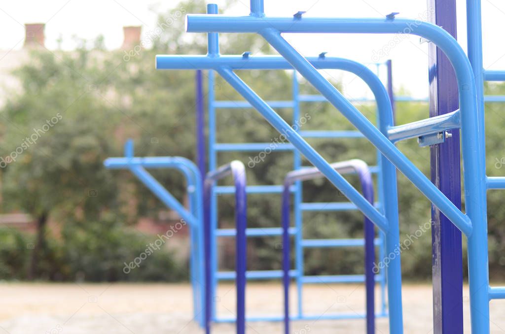 Sports bars in blue on the background of a street sports ground for training in athletics. Outdoor athletic gym equipment. Macro photo with selective focus and extremely blurred background