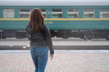 Kızıl saçlı bir kız demiryolu platformu üzerinde duran ve çıkış yapan tren izliyor. Treni için geç bir kadındı. Arkadan Görünüm