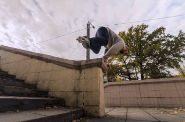 Genç bir adam bir atlama beton parapetin üzerinden gerçekleştirir. Sokak koşullarda eğitim atlet uygulamaları parkour. Spor altkültürler gençler arasında kavramı