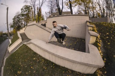 Genç bir adam bir atlama beton parapetin üzerinden gerçekleştirir. Sokak koşullarda eğitim atlet uygulamaları parkour. Spor altkültürler gençler arasında kavramı