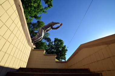 Genç bir adam uzayda atlama Beton korkuluk arasında gerçekleştirir. Sokak koşullarda eğitim atlet uygulamaları parkour. Alt görünümü