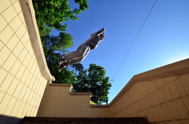 Genç bir adam uzayda atlama Beton korkuluk arasında gerçekleştirir. Sokak koşullarda eğitim atlet uygulamaları parkour. Alt görünümü