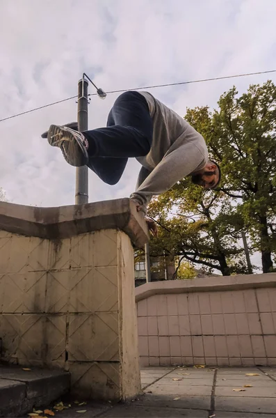 A young guy performs a jump through the concrete parapet. The athlete practices parkour, training in street conditions. The concept of sports subcultures among youth
