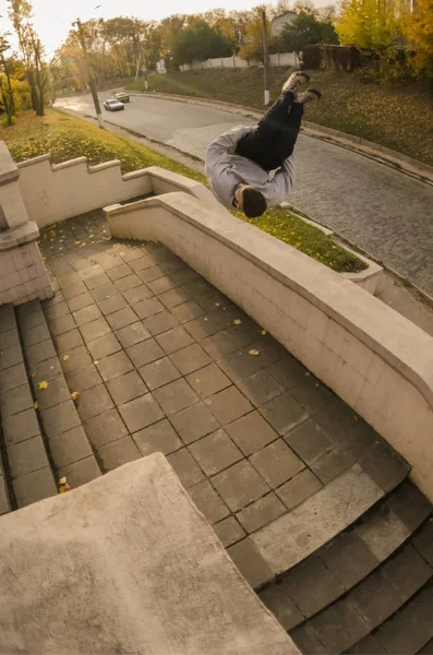 A young guy performs a side flip in the autumn park. The athlete practices parkour, training in street conditions. The concept of sports subcultures among youth