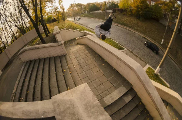 A young guy performs a side flip in the autumn park. The athlete practices parkour, training in street conditions. The concept of sports subcultures among youth