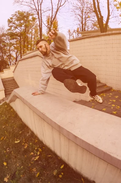 A young guy performs a jump through the concrete parapet. The athlete practices parkour, training in street conditions. The concept of sports subcultures among youth