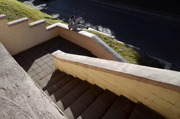 A young guy performs a jump through the concrete parapet. The athlete practices parkour, training in street conditions. The concept of sports subcultures among youth