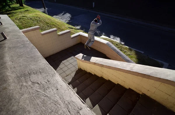 A young guy performs a jump through the space between the concrete parapets. The athlete practices parkour, training in street conditions. The concept of sports subcultures among youth