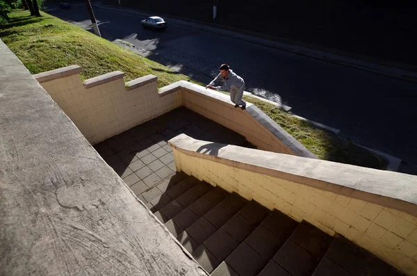 A young guy performs a jump through the space between the concrete parapets. The athlete practices parkour, training in street conditions. The concept of sports subcultures among youth