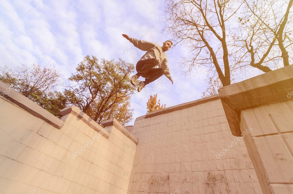 A young guy performs a jump through the space between the concrete parapets. The athlete practices parkour, training in street conditions. The concept of sports subcultures among youth