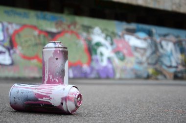 Birkaç kullanılan sprey kutular pembe ve beyaz boya ile renkli grafiti çizimlerinde boyalı duvar arka planı asfalt üzerinde yalan