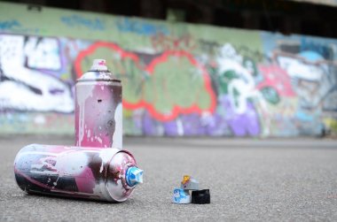 Pembe ve beyaz boya ve baskı altında boya püskürtme için kapaklar ile çeşitli kullanılan sprey kutular renkli grafiti çizimler boyalı duvarın yanında asfalt üzerinde yalan olduğunu
