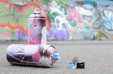 Pembe ve beyaz boya ve baskı altında boya püskürtme için kapaklar ile çeşitli kullanılan sprey kutular renkli grafiti çizimler boyalı duvarın yanında asfalt üzerinde yalan olduğunu
