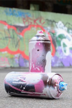 Pembe ve beyaz boya ve baskı altında boya püskürtme için kapaklar ile çeşitli kullanılan sprey kutular renkli grafiti çizimler boyalı duvarın yanında asfalt üzerinde yalan olduğunu