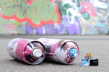Pembe ve beyaz boya ve baskı altında boya püskürtme için kapaklar ile çeşitli kullanılan sprey kutular renkli grafiti çizimler boyalı duvarın yanında asfalt üzerinde yalan olduğunu