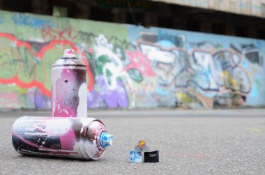 Pembe ve beyaz boya ve baskı altında boya püskürtme için kapaklar ile çeşitli kullanılan sprey kutular renkli grafiti çizimler boyalı duvarın yanında asfalt üzerinde yalan olduğunu