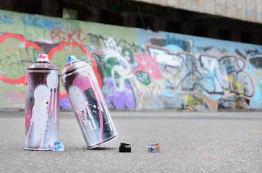 Pembe ve beyaz boya ve baskı altında boya püskürtme için kapaklar ile çeşitli kullanılan sprey kutular renkli grafiti çizimler boyalı duvarın yanında asfalt üzerinde yalan olduğunu