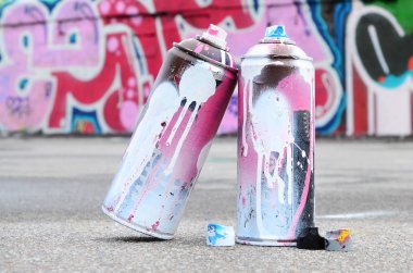 Pembe ve beyaz boya ve baskı altında boya püskürtme için kapaklar ile çeşitli kullanılan sprey kutular renkli grafiti çizimler boyalı duvarın yanında asfalt üzerinde yalan olduğunu
