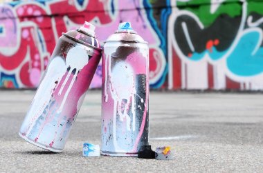 Pembe ve beyaz boya ve baskı altında boya püskürtme için kapaklar ile çeşitli kullanılan sprey kutular renkli grafiti çizimler boyalı duvarın yanında asfalt üzerinde yalan olduğunu